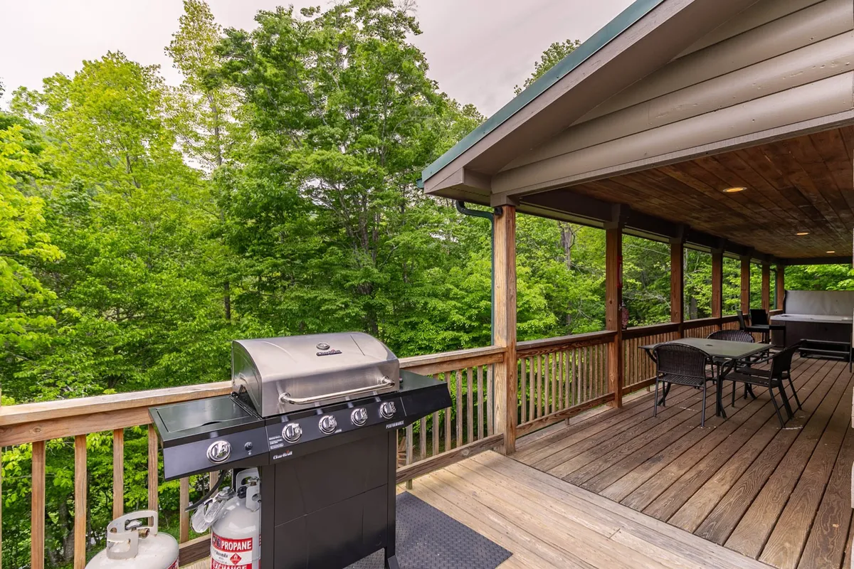 A covered deck featuring a grill, comfortable deck furniture, and lush greenery all around. The space is casual yet inviting, ideal for grilling and enjoying meals outdoors while taking in the sounds of the nearby creek.