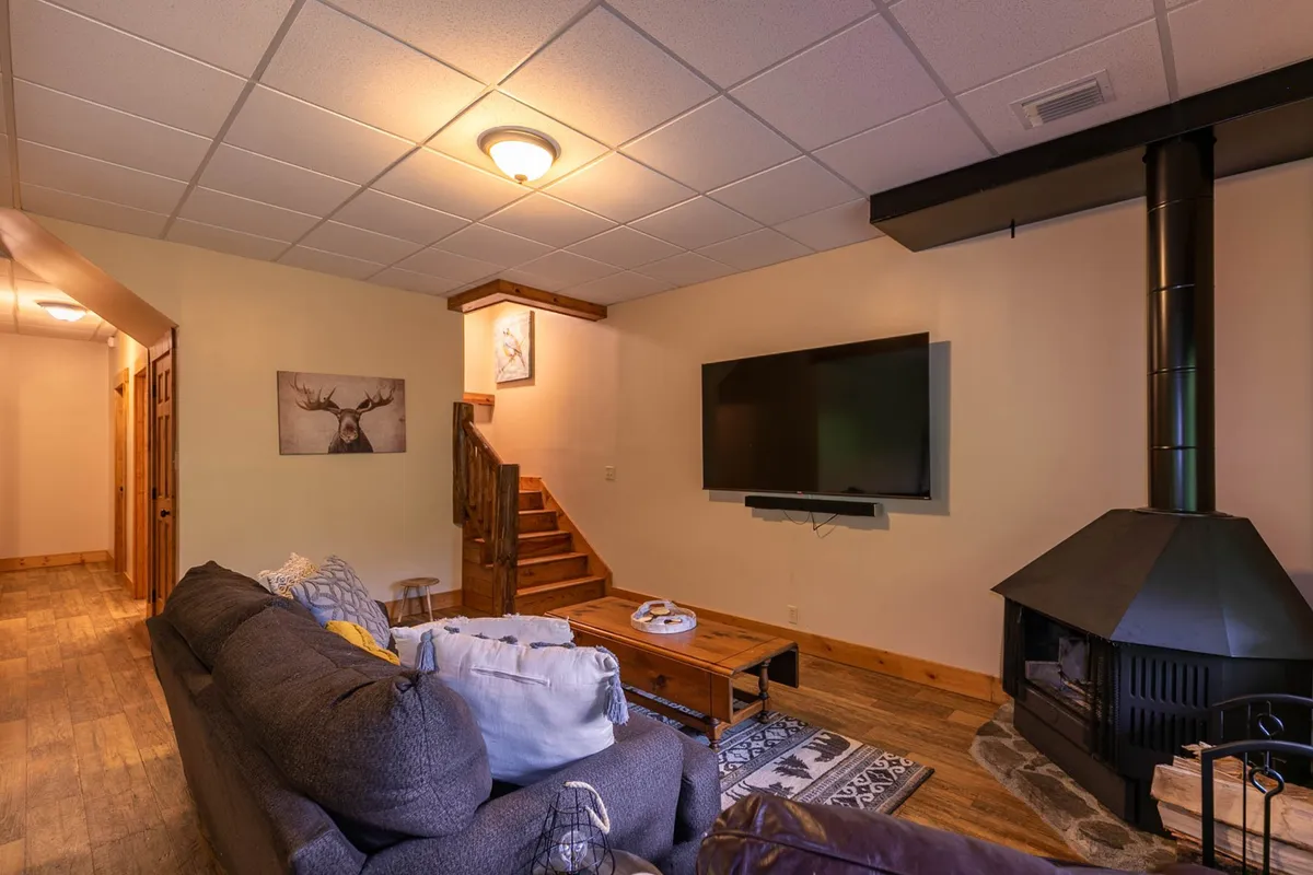 This image highlights a cozy corner with a sofa, fireplace, TV, and stairs leading to other levels of the home. Artwork and soft lighting complete the inviting, family-oriented vibe of the room.