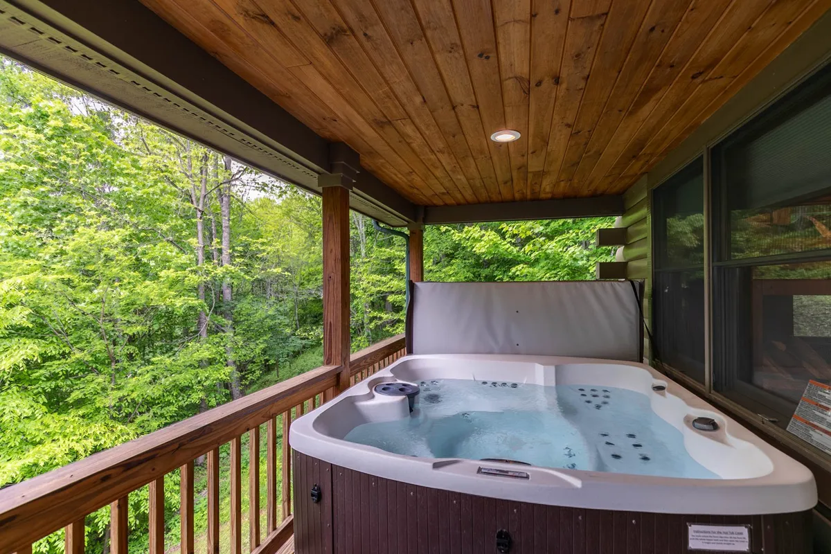 A tranquil wooden deck featuring a bubbling hot tub, surrounded by dense greenery and forest. The setting invites relaxation after outdoor activities, with sunset light filtering through the trees, emphasizing the connection between adventure and restorative comfort.