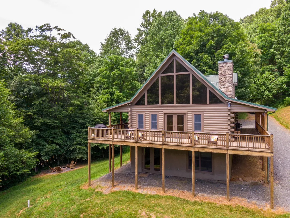 An inviting exterior view of the cabin reveals large glass windows, a prominent stone chimney, and a wooden deck poised for gatherings. The sunset light creates a tranquil mood, enhancing the sense of a comfortable home base between excursions.