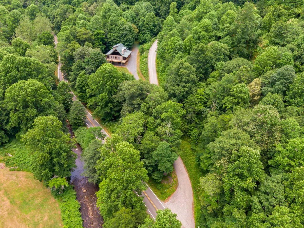 An exterior view of the house nestled alongside a winding road, with the creek and surrounding trees visible. The natural setting is tranquil and highlights the property's creekside location and abundance of outdoor adventure possibilities.