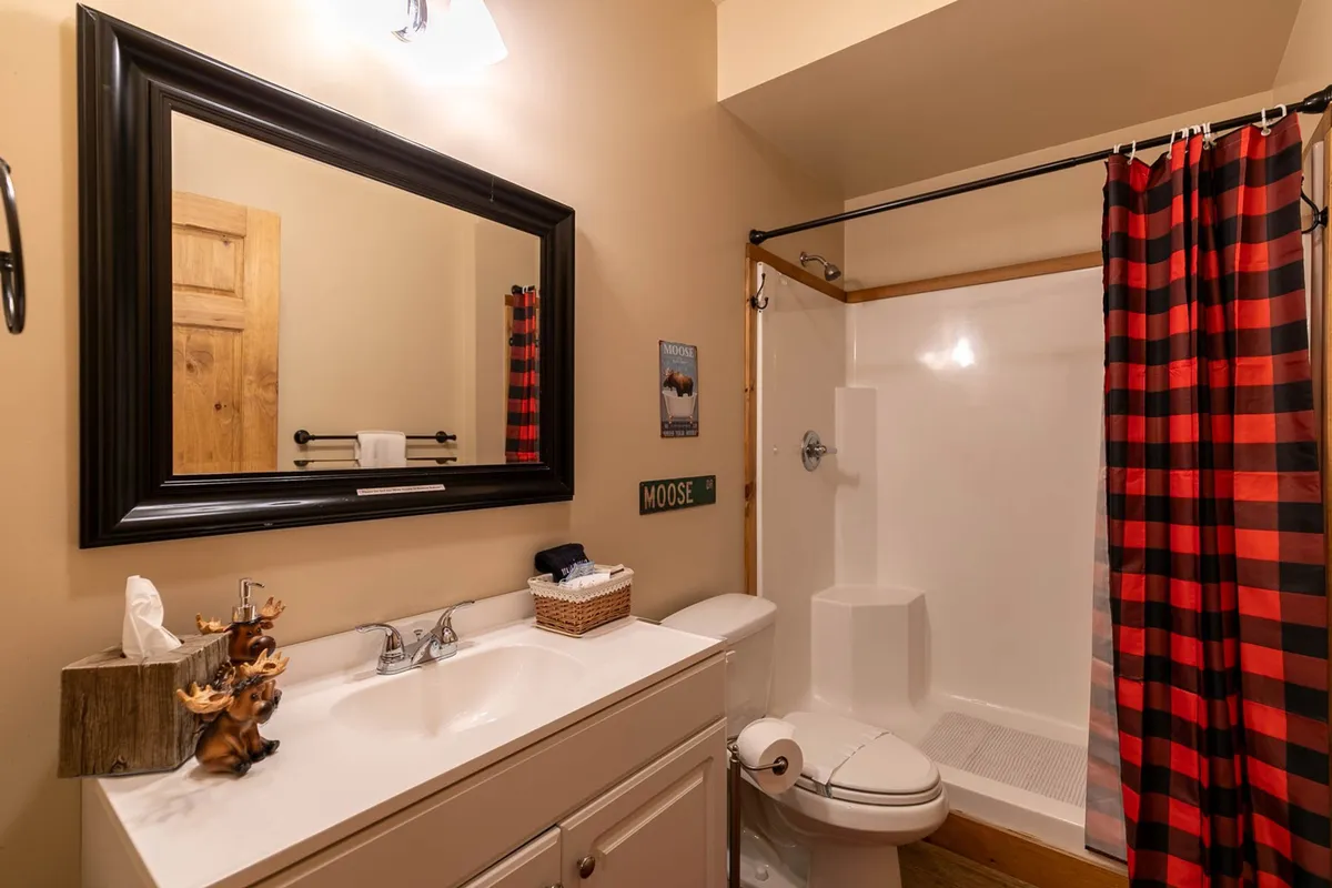 A modern bathroom with a large mirror, granite vanity, sink, and an inviting shower with a curtain. Rustic decor, including a decorative moose figurine, adds a touch of local charm.