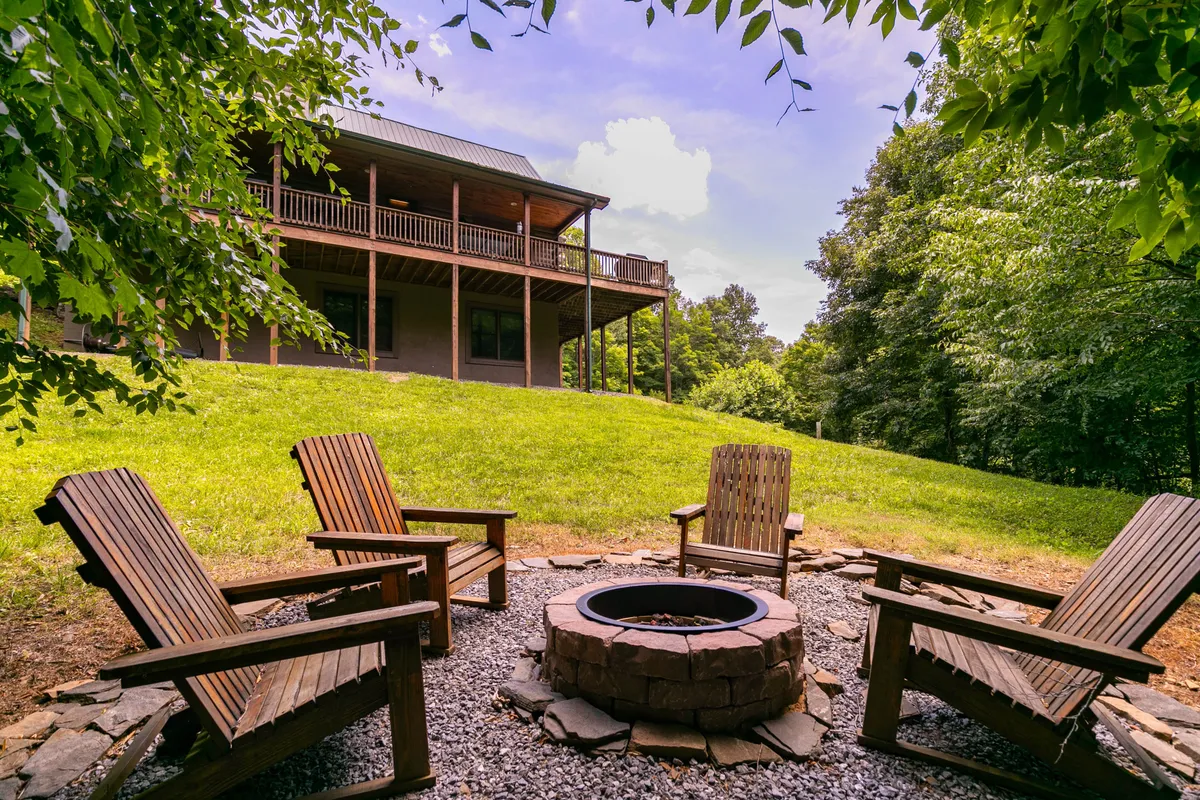 This scene centers on a cozy fire pit surrounded by wooden chairs and backed by the porch of the house. The environment is perfect for gathering, stargazing, and enjoying the warmth of a fire as dusk falls.