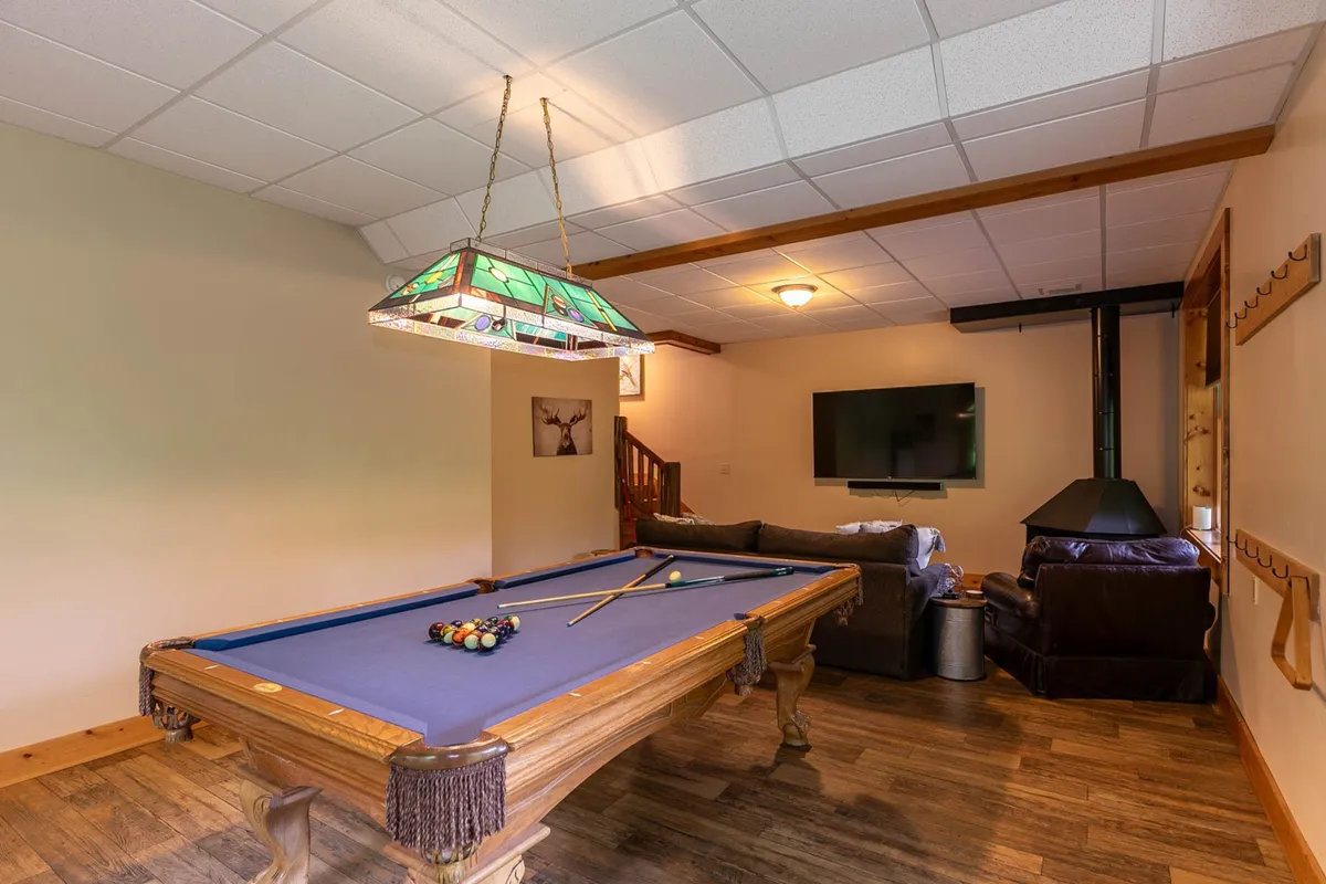 The image captures a lively game den featuring a pool table under a stained glass lamp, a comfortable seating area, and a television prominently displayed on the wall. The warm lighting and casual furnishings create an inviting environment ideal for friendly competition and relaxation.