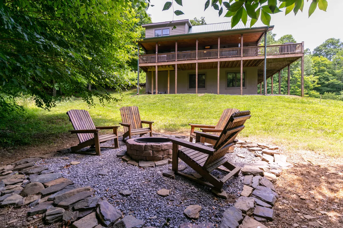 A cozy fire pit ringed by Adirondack chairs on the deck, with the house in the background. The scene suggests warm evening gatherings, stargazing, and sharing stories after a day of mountain activities.